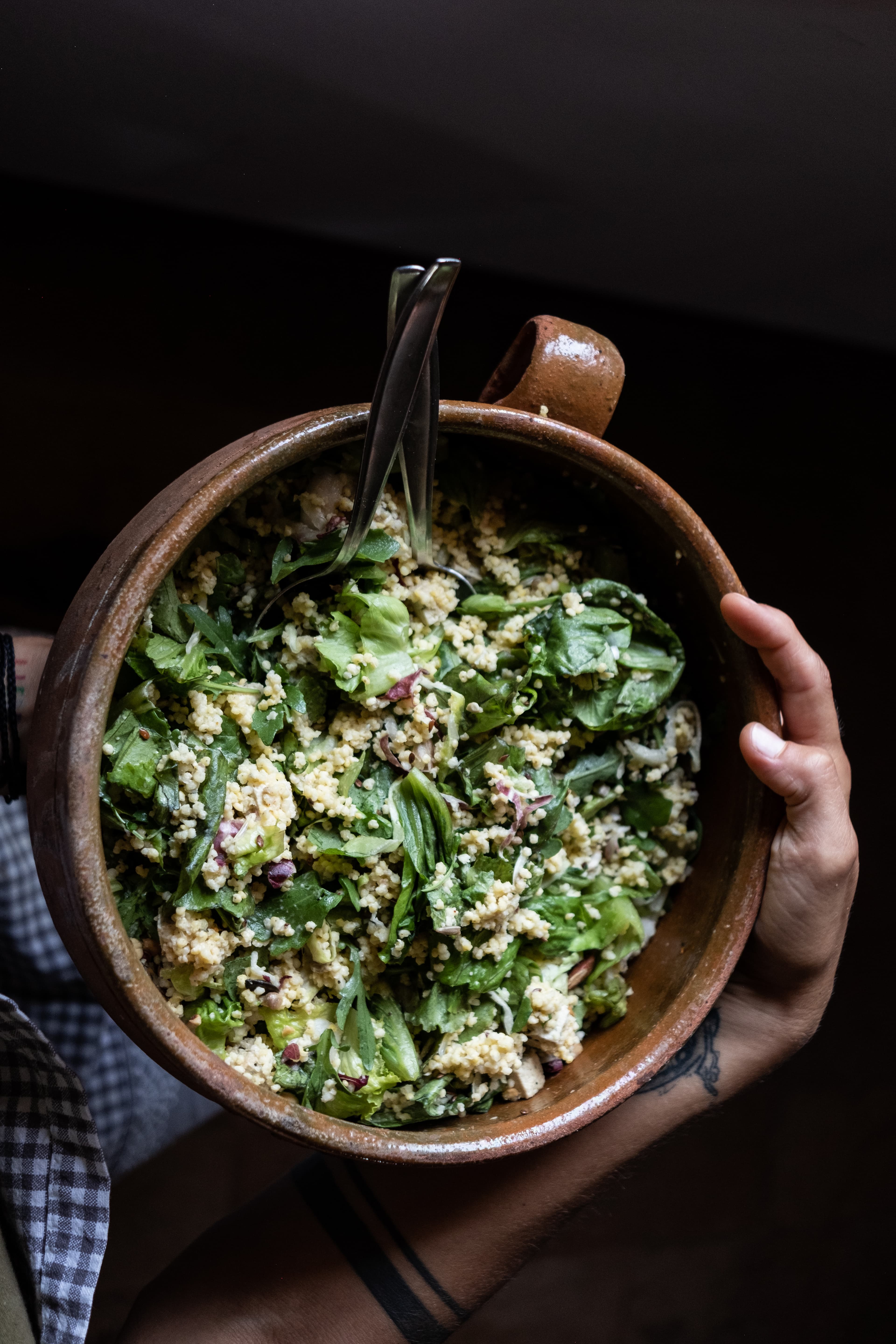 Person holding a rustic brown ceramic bowl filled with vibrant green salad