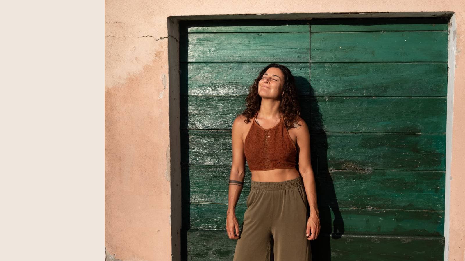 Woman with curly dark brown hair in rust-colored top against textured wall and teal door